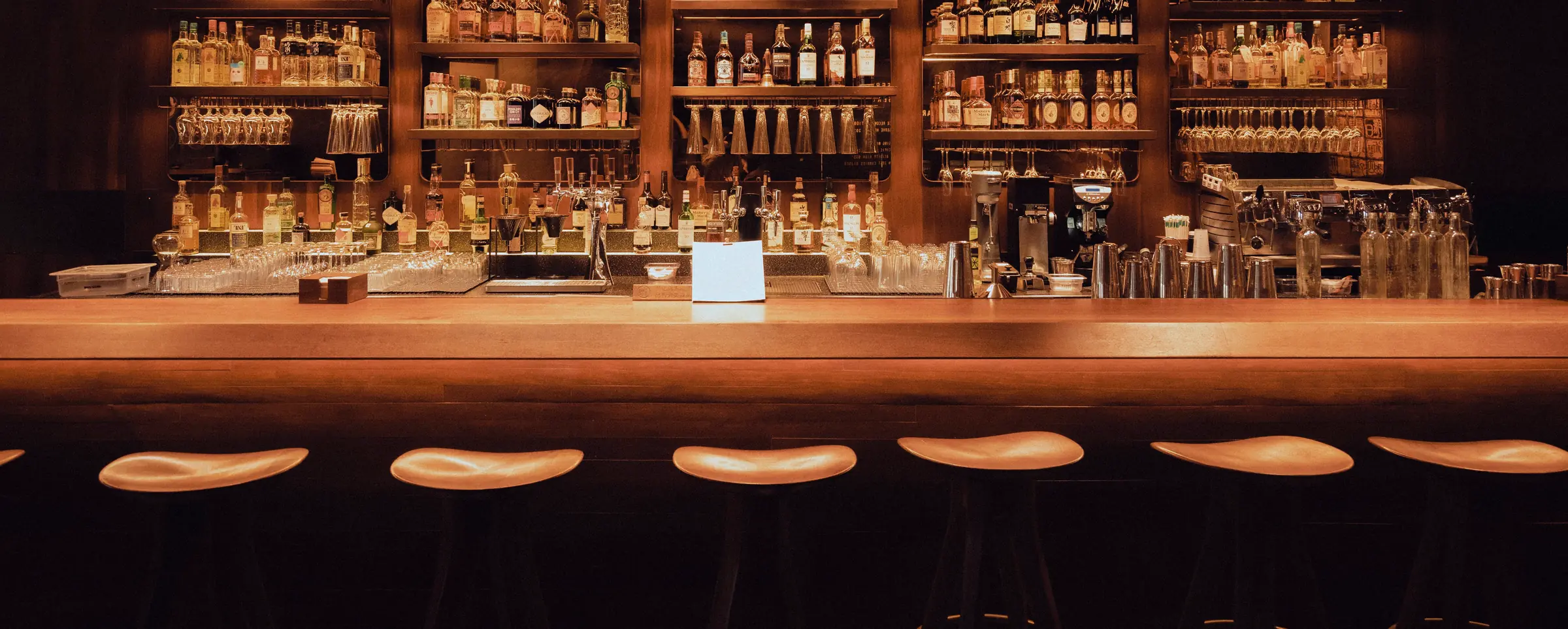 A warm wood bar with a full back bar of bottles